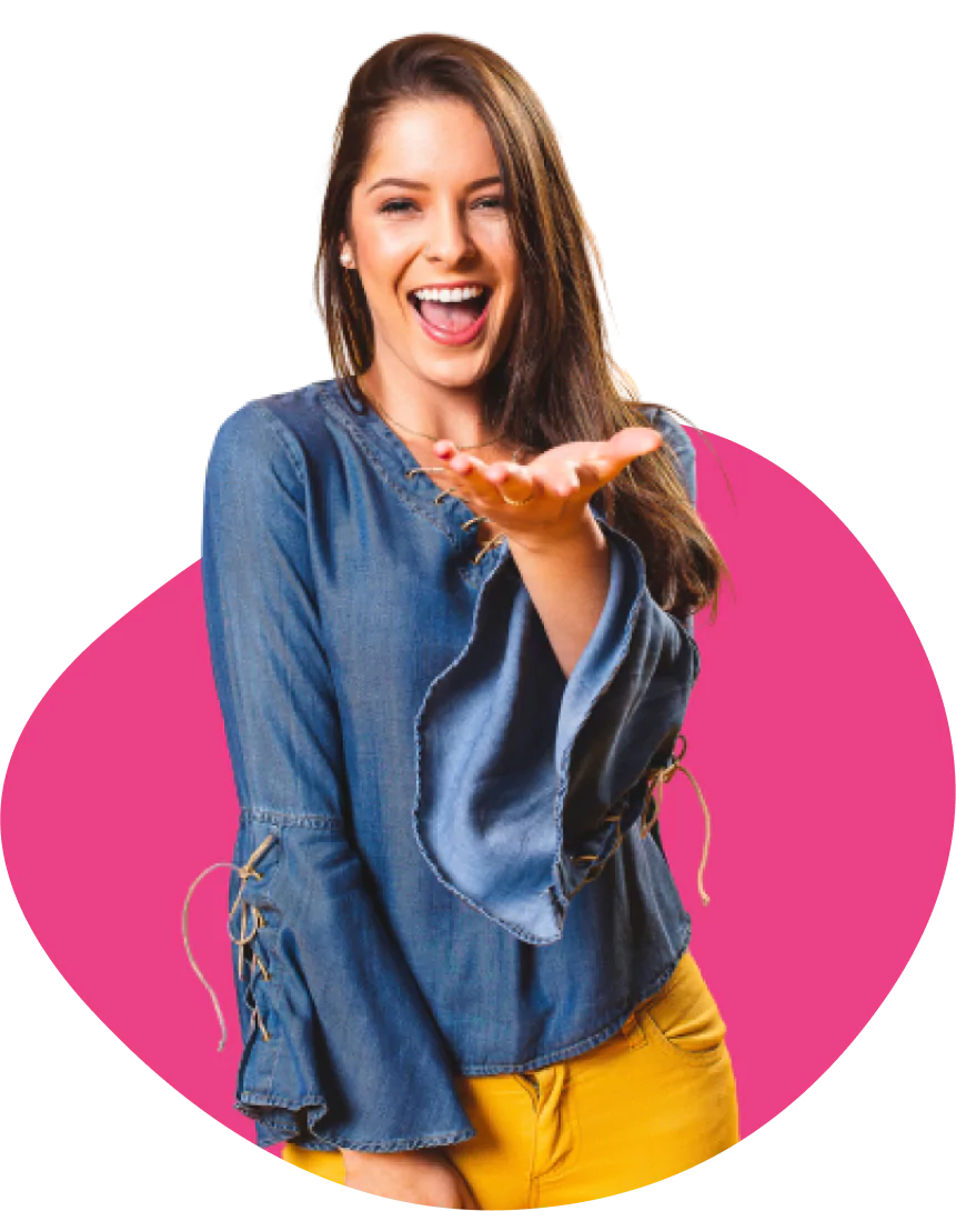 A smiling young woman with long brown hair, wearing a denim top and yellow pants, extending her hand forward as if presenting or inviting